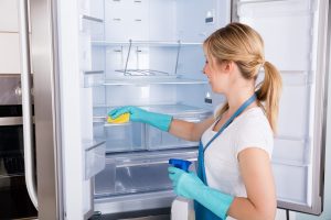 Young,Smiling,Professional,Janitor,Woman,Cleaning,Empty,Refrigerator,In,Kitchen